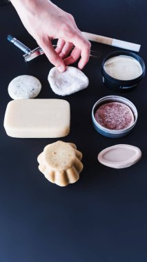 Bir kadının eli siyah arka plandaki çeşitli ekolojik nesneler arasında yeniden kullanılabilir bir makyaj sökücü diski alır.