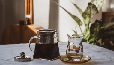 Yumuşak pastel bir çaydanlık sahnesi, sıcak çay ve masada klasik Türk çay bardağı.