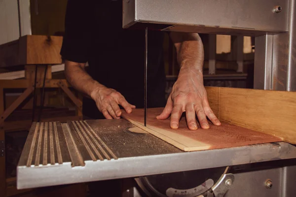 Bir erkek marangoz atölyede testereyle tahta kesiyor.