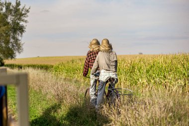 İki kişi mısır tarlasında bisiklet sürüyor.