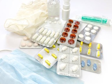 Farklı ilaçlar: tabletler, su toplayan haplar, ilaçlar ilaçlar, tıbbi eldivenler, maske, şırınga, termometre, sprey, beyaz arka planda dezenfektan. Yatay fotoğraf