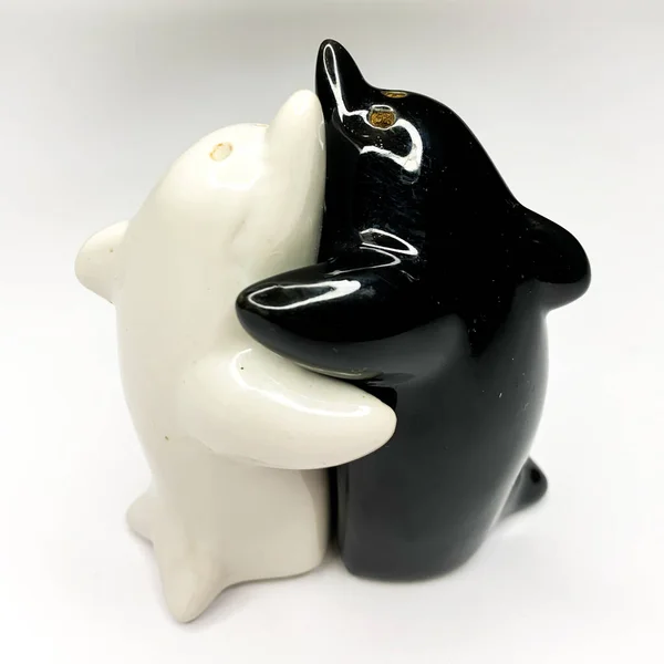 Black and white yin yang dolphin shaped salt and pepper shakers hugging each other on white background