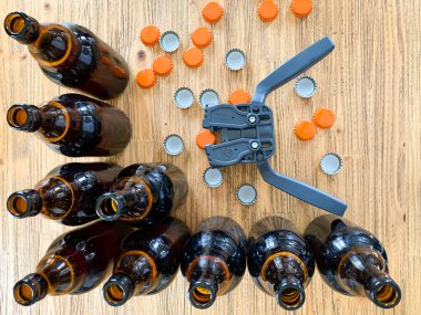 Evde bira demleme, şişelerin üzerine metal kapaklar, kahverengi cam bira şişeleri ve ahşap arka planda turuncu taç kapakları koymak için plastik kaplama, yatay görüntü