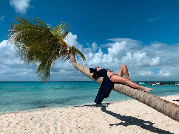 Bikini ve mavi pareolu güneş gözlüklü güzel, mutlu, Avrupalı kız Dominik Cumhuriyeti 'nin Saona adasındaki beyaz kumsalda hindistan cevizi palmiyesinde yatıyor. Tatil resmi