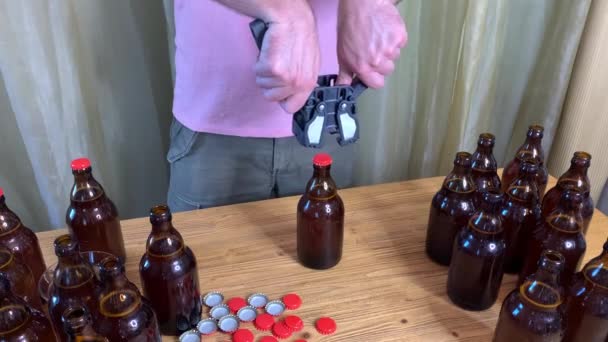 自宅でクラフトビール醸造 男は赤い冠キャップと木製のテーブルの上にプラスチックキャップと茶色のガラスビールボトルを閉じます 水平Hdストックビデオを閉じる — ストック動画