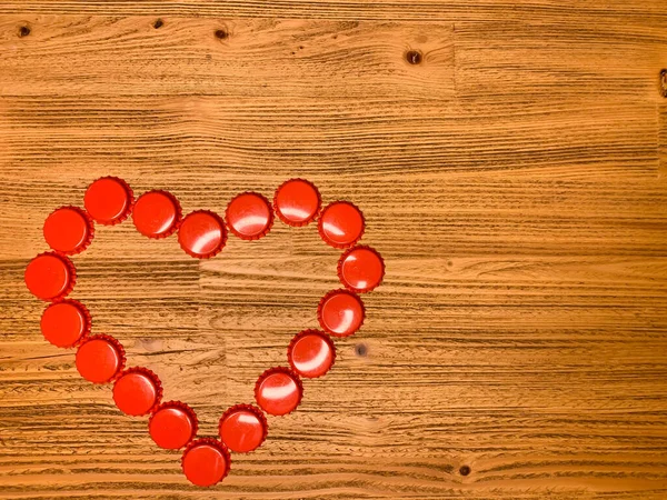 Red love heart made from beer bottle tops lids on a rustic wooden table. Beer drinkers Valentine\'s day concept, top view horizontal stock image with empty space for text