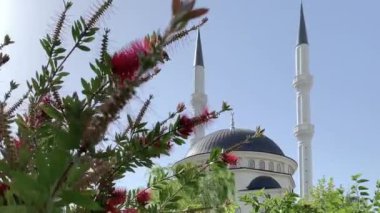 Türkiye 'de güneşli bir günde kırmızı çiçekli, mavi gökyüzü arka planlı yeni bir güzel beyaz cami. 4k stok video.