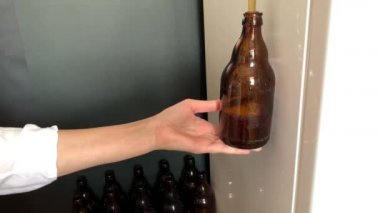 El yapımı bira fabrikası. Evde kahverengi cam bira şişelerini dolduran bir kadın eli. Kendi yapımı bira HD stok videosu.