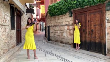 Sarı konser elbiseli iki genç kız kardeş kemancı, eski Antalya Kaleici Türkiye 'nin küçük güzel tarihi bir caddesinde elektrikli kemanlar çalıyorlar. 4k stok video.