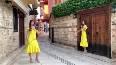 Sarı konser elbiseli iki genç kız kardeş kemancı, eski Antalya Kaleici Türkiye 'nin küçük güzel tarihi bir caddesinde elektrikli kemanlar çalıyorlar. 4k stok video.