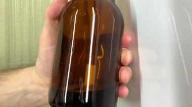 El yapımı bira fabrikası. Evdeki kahverengi cam bira şişelerini dolduran erkeğin elini kapat. Kendi yapımı bira 4K stok video.