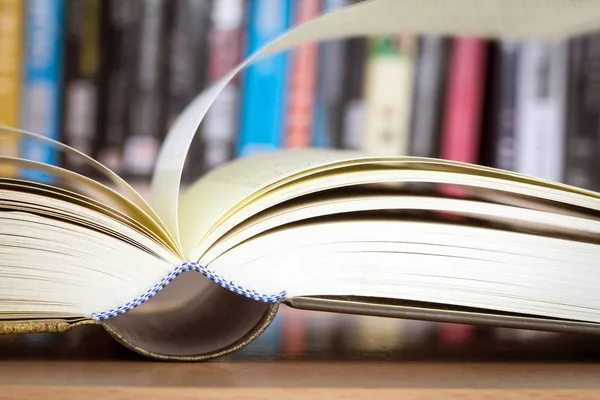 Close up opened book page with blurry bookshelf background — Stock Photo, Image