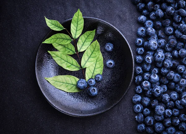 Fresh picked blueberries with green of leaf on black stone back — Stock Photo, Image