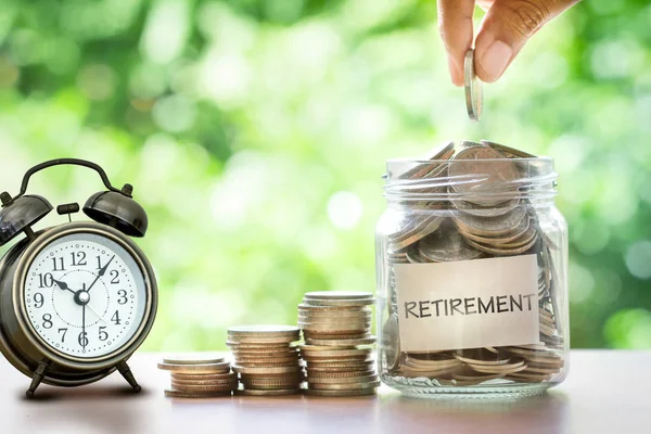 Hand putting Coins in glass jar with retro alarm clock — Stock Photo, Image