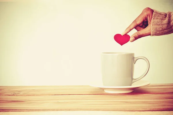 Ruka držící tvar červené srdce, dát do hrnku šálek kávy na zalesněný — Stock fotografie