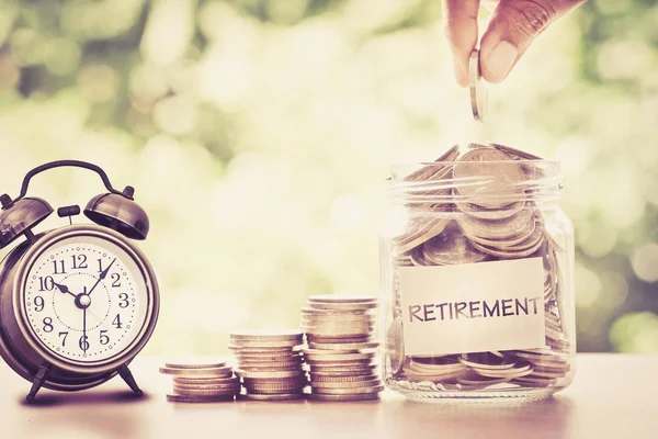 Hand putting Coins in glass jar with retro alarm clock