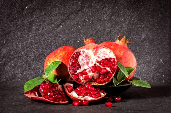 Melograno rosso fresco e semi con foglie sopra bac pietra nera — Foto Stock