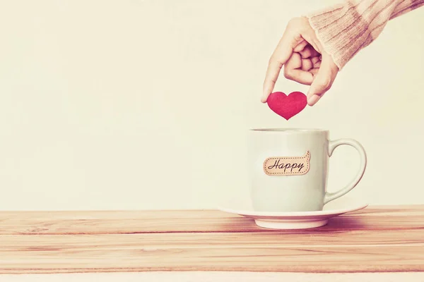 Ruka držící červené srdce tvar do hrnečku šálek kávy s hap — Stock fotografie