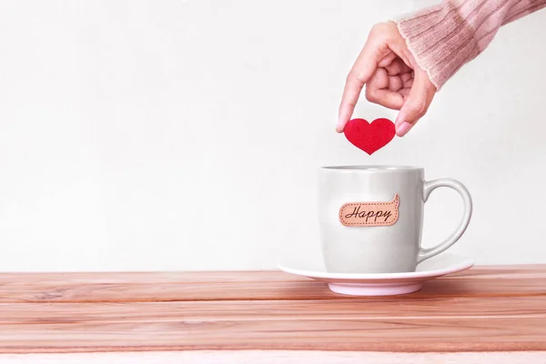 Ruka držící červené srdce tvar do hrnečku šálek kávy s hap — Stock fotografie