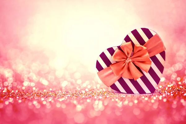 La scatola regalo a forma di cuore rosso su brillantini leggeri astratti — Foto Stock
