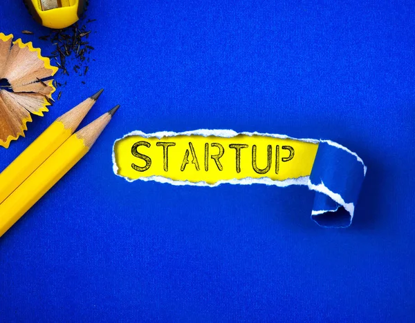 El lápiz amarillo sobre papel azul rasgado y palabra STARTUP con un ye — Foto de Stock