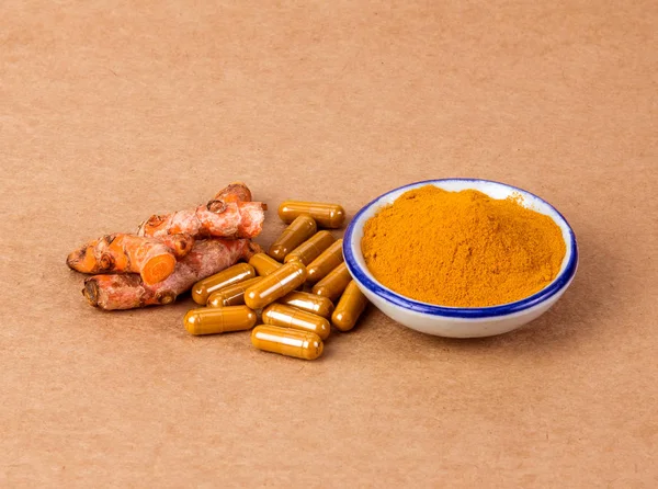 turmeric powder and capsule and roots curcumin on brown paper