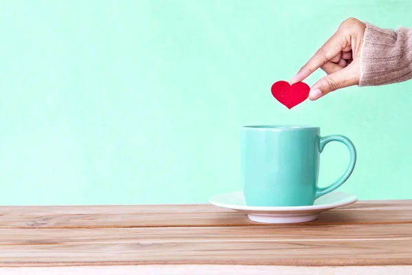 Ruka držící tvar červené srdce, dát do hrnku šálek kávy na zalesněný — Stock fotografie