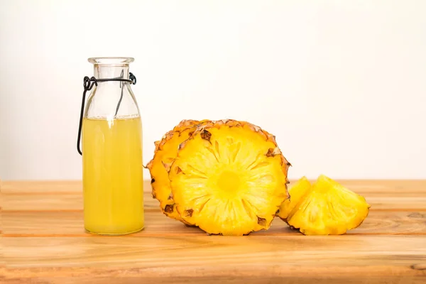 Bottles of pineapple juice with a sliced pineapple fruit on wood — Stock Photo, Image