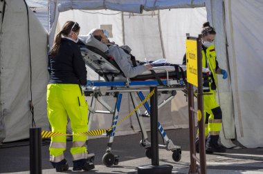 Milano, İtalya - 11 Mart 2020. Koruyucu maskeli sağlık görevlileri Corona Virüsü taşıyan bir adama triyaj hastanesi çadırı dışında sedyede yatarken yardım ediyor. 2019-Ncov için küresel uyarı uyarısı.