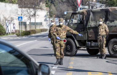 Askerler kontrol eder. Maskeli ve eldivenli güvenlik devriyesi geçen sürücüleri izliyor. Covid-19 küresel krizi için günlük sokak kontrolü. Ordu iş başında..