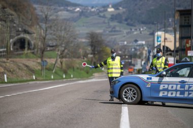 Bozen, İtalya - 23 Nisan, 2020. İtalyan polisi yolu kontrol ediyor. Maskeli ve eldivenli memurlar geçen sürücüleri izliyor. Covid-19 için bir kadın polisle sokak kontrolü. Polis kontrol noktası.