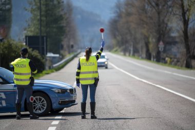 Bozen, İtalya - 23 Nisan, 2020. İtalyan polisi yolu kontrol ediyor. Maskeli ve eldivenli memurlar geçen sürücüleri izliyor. Covid-19 için bir kadın polisle sokak kontrolü. Polis kontrol noktası.