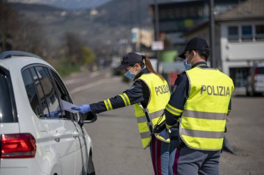 Bozen, İtalya - 14 Mayıs 2020. Corona Virüsü uyarısı. İtalyan polisi yolu kontrol ediyor. Maskeli ve eldivenli memurlar geçen sürücüleri izliyor. Covid-19 için bir kadın polisle sokak kontrolü..