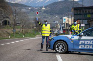 Bozen, İtalya - 23 Nisan, 2020. İtalyan polisi yolu kontrol ediyor. Maskeli ve eldivenli memurlar geçen sürücüleri izliyor. Covid-19 için bir kadın polisle sokak kontrolü. Polis kontrol noktası.