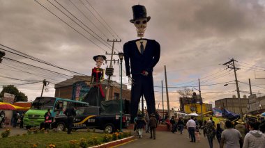 Muecos gigantes con forma de esqueletos (catrina y catrino) ubicados en medio de la calle de un pequeo poblado lleno de gente para dar la bienvenida a todos turistas que llegan por motive os da muertos.