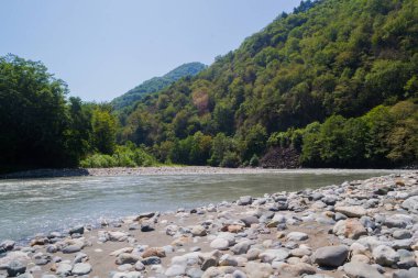 Dağlarda dağ nehri, ön planda kayalar.