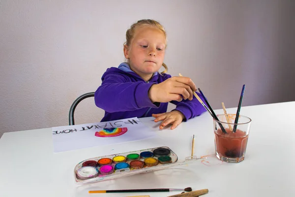 Girl draws a rainbow of hope with the words stay home