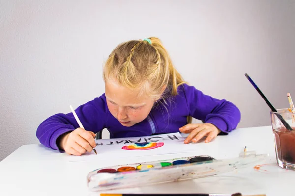 Girl draws a rainbow of hope with the words stay home