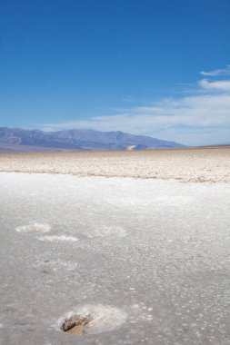 ÖIüm Vadisi Ulusal Parkı 'ndaki Badwater Havzası' nda, ön planda doğal bir delik, beyaz tuzlu zeminde ayak izleri yaratıyor.