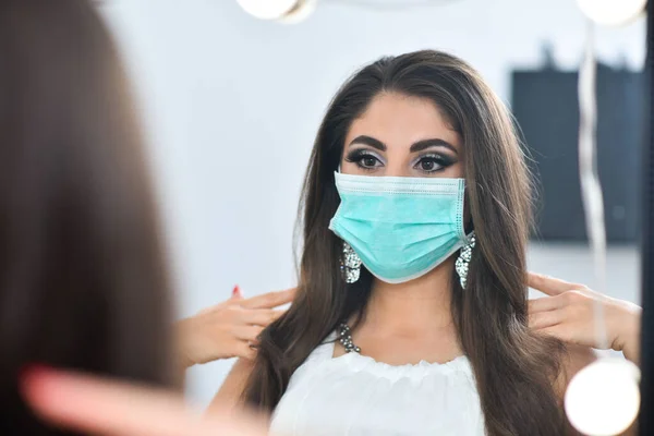 Medical mask and a beautiful girl. Female beauty and mask. Girl puts on mask near the mirror. Medical concept.