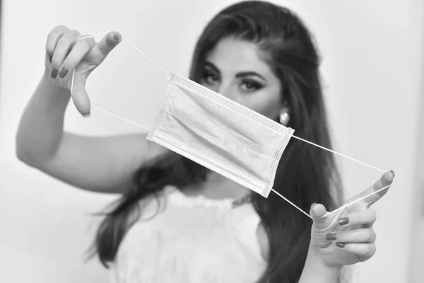 Girl holds a medical mask on a light background. The girl is holding a mask. Mask and a beautiful girl. Coronavirus concept. Female beauty and mask.