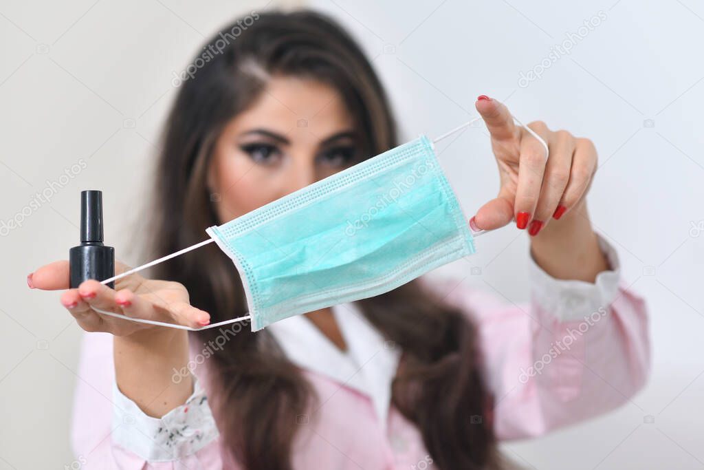 Girl holds a medical mask on a light background. The girl is holding a mask. Mask and a beautiful girl. Coronavirus concept. Female beauty and mask.