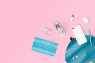 Koruyucu tıbbi maske de dahil olmak üzere kadın çantasının içindeki gerekli eşyaların düz yerleşimi. Pembe arkaplan