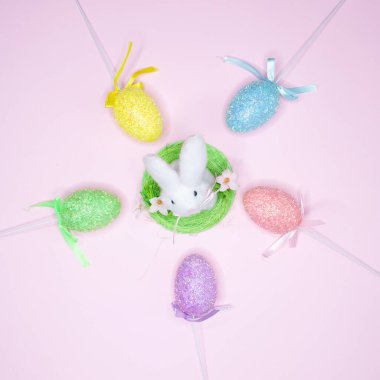 Renkli boyalı yumurtalar ve pembe arka planda Paskalya tavşanı.