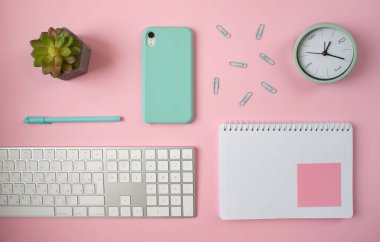 Pembe zemin üzerinde kalem, klavye ve bitkiyle boş not defterinin düz düzeni