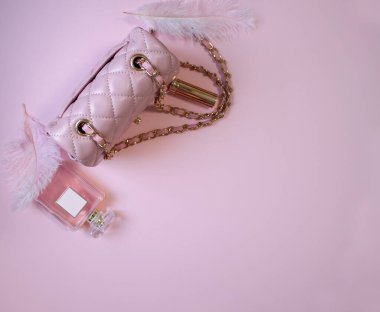Düz bir çanta ve pembe arka planda bir şişe parfüm.
