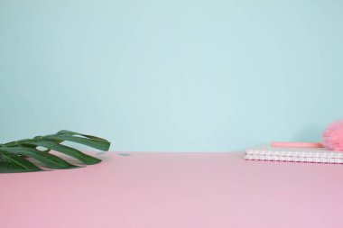 Durgun bir hayatın yan görüntüsü. Yeşil canavar yaprağı, not defteri ve kalem parlak pembe ve nane arkaplanda.. 