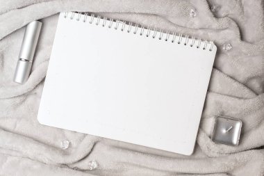 Boş not defteri, kozmetik şişe ve gri kürk arka planda bir mum.