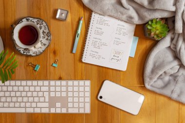 Konforlu işyerinin düz yatağı. Ahşap arkaplanda planlayıcı, klavye, telefon ve çay.