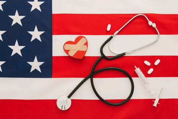 Medical concept flat lay of a stethoscope, pills and vaccines near to a heart on American flag as background and copy space